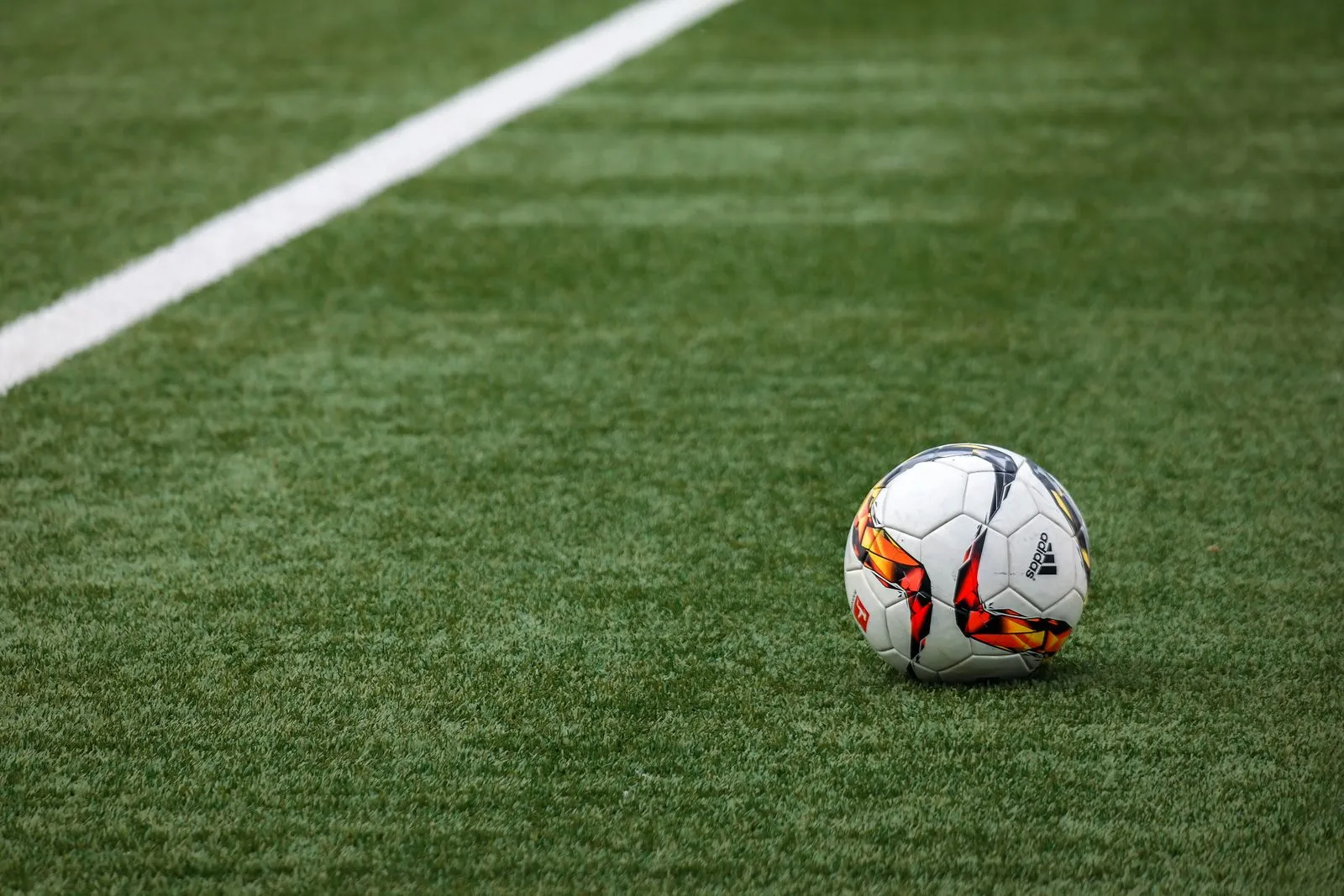 Bola de futebol parada no gramado ao lado da linha branca do campo